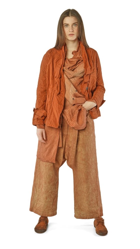 Person trägt oversized orangefarbene Jacke, gestreiften Schal und weite beige Hosen mit Anzugscharakter.