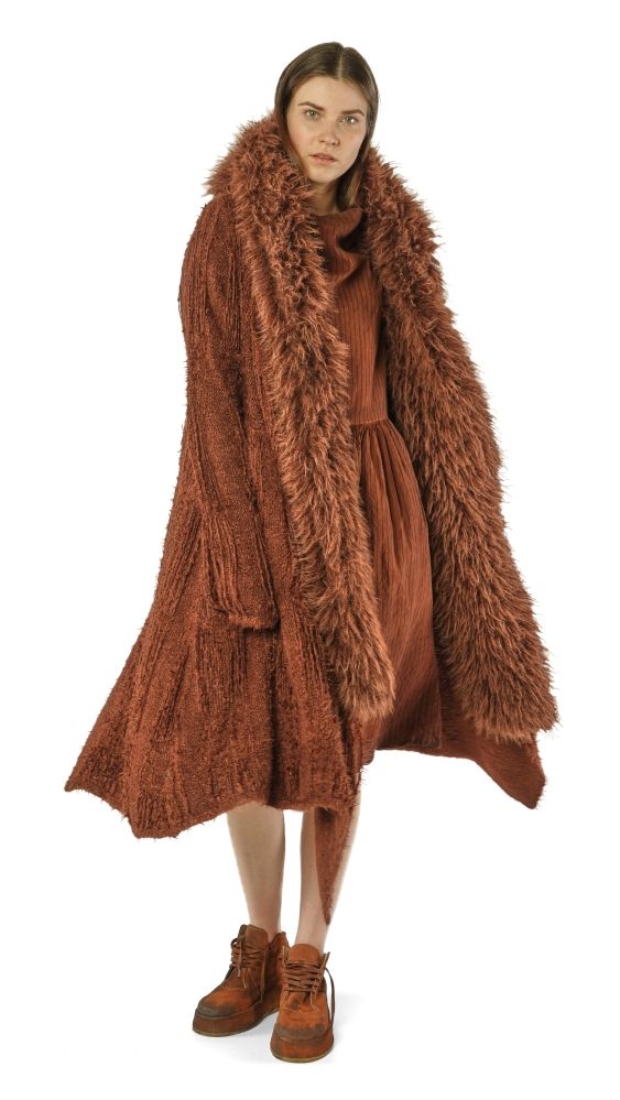 Frau trägt langen, braunen, flauschigen Mantel mit Fellkragen und kurze Stiefel.