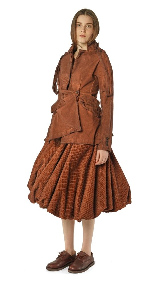 Frau trägt rustikales, braunes oversized Kleid mit weitem Rock und Weste, barfuß mit Schuhen.