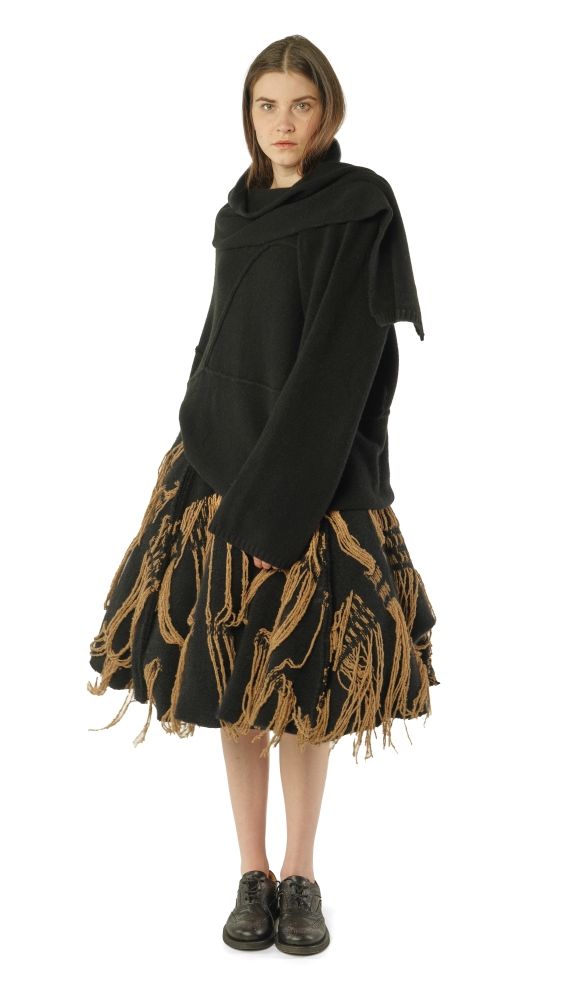 Frau trägt oversized schwarzen Pullover mit Fransenrock und schwarzen Stiefeln.
