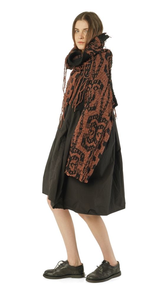 Frau trägt oversized schwarzen Mantel mit rot-schwarzem Schal, kurze Hose und schwarze Sneaker.