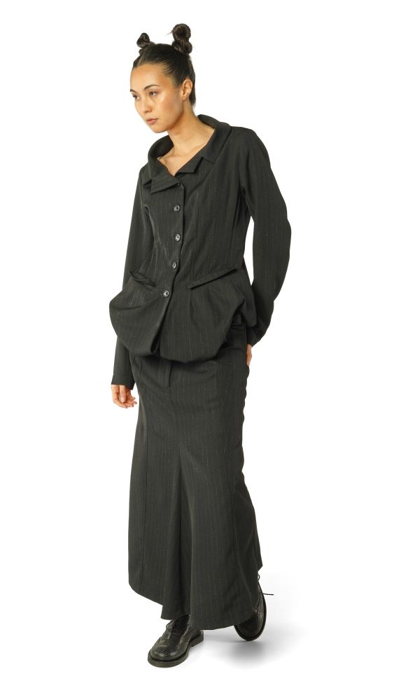 Frau trägt oversized schwarzen Blazer mit weitem Rock und schwarzen Sneakern, Haare zu zwei Knoten gebunden.
