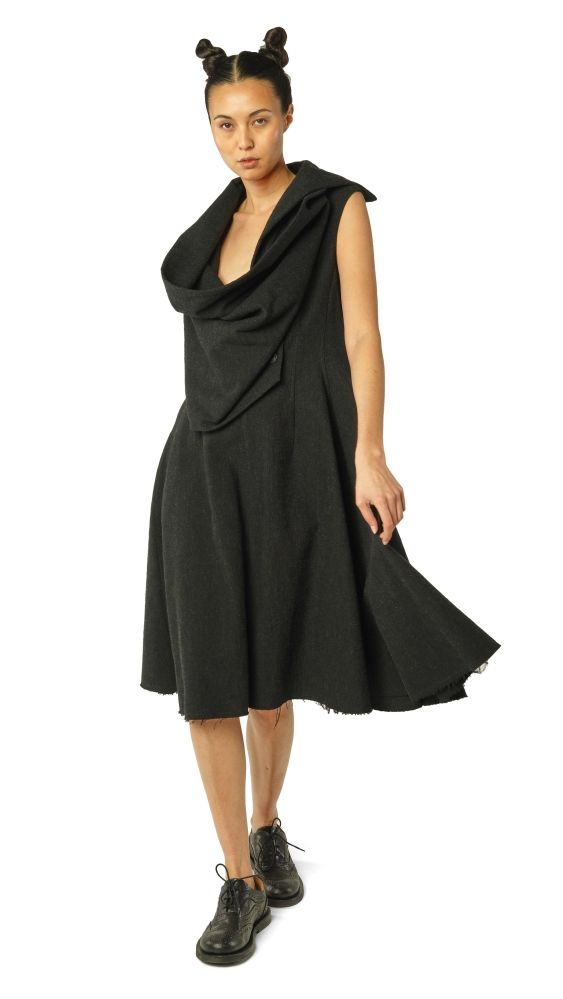 Frau trägt elegantes schwarzes oversized Kleid mit asymmetrischen Details und schwarzen Stiefeln.