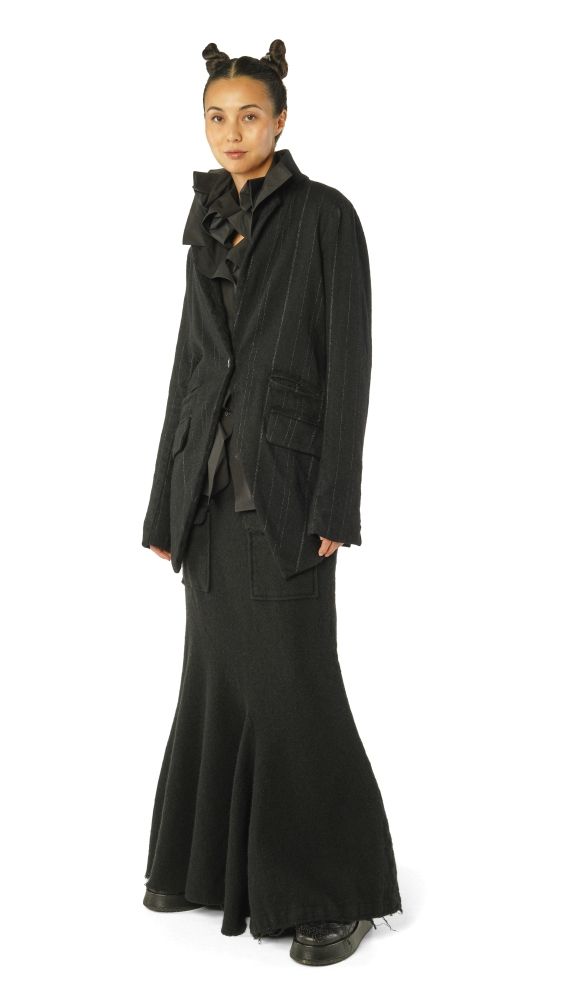 Frau trägt elegantes, langes schwarzes Cape-Kleid mit asymmetrischen Details und Bum-Bums-Frisur.
