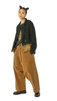 Person trägt oversized schwarze Jacke, karierte Weste und weite beige Hosen mit Accessoires.