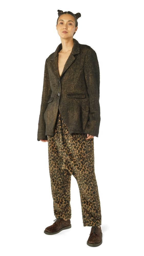 Person trägt oversized Tweedjacke, leopardbedruckte Hosen und braune Stiefel mit Katzenohren-Haarspange.