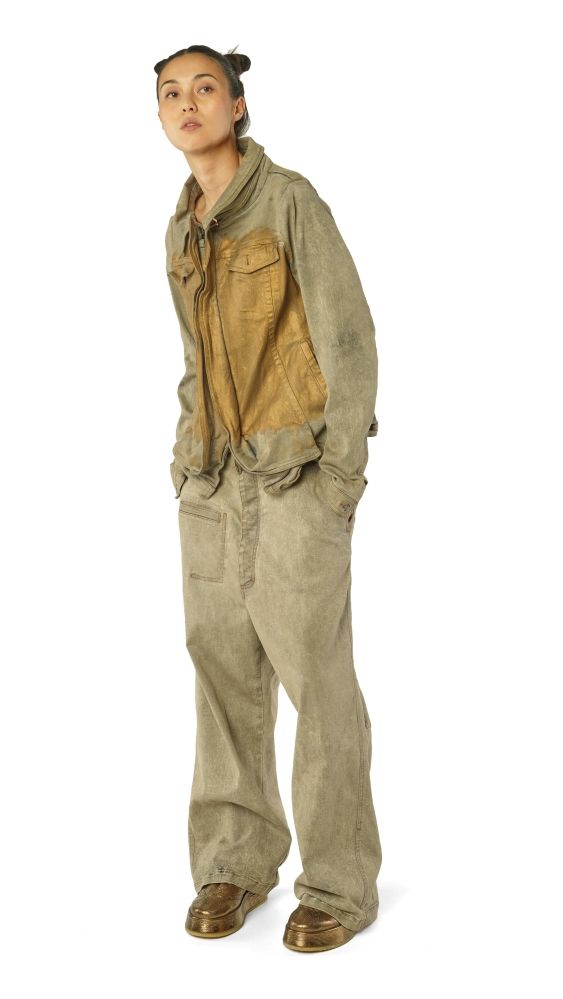 Person in abgetragenen Overall-Hose und Jacke, nachdenklich blickt nach oben.
