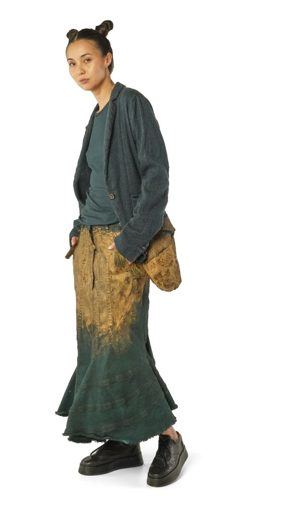 Person trägt oversized Jacke, bunte weite Hose und schwarze Sneaker, Haar zu zwei Buns gebunden.