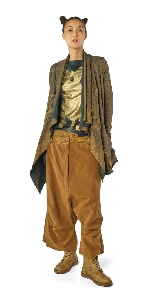 Person trägt bunte, oversized Kleidung mit goldener Weste, braunen Hosen und Bärenohren-Haarreif.