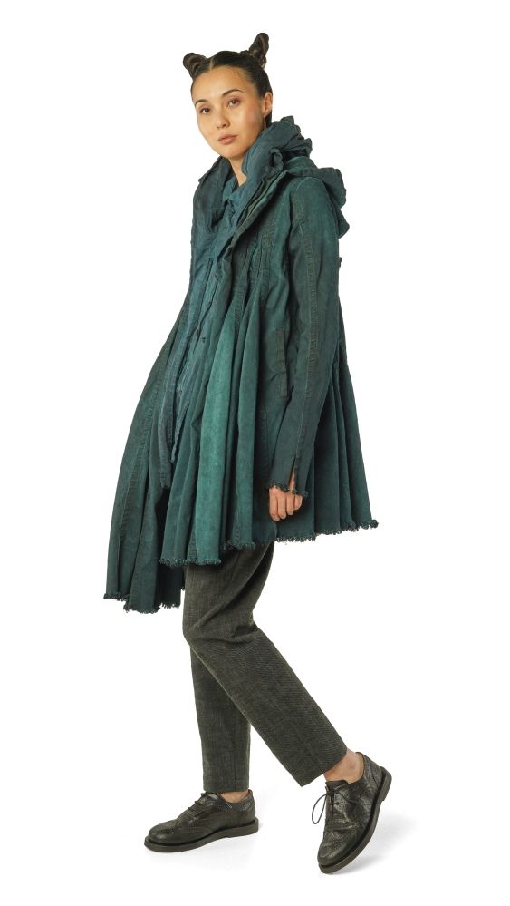 Person trägt oversized grünen Mantel mit Fellkragen, schwarze Hose und Schuhe.