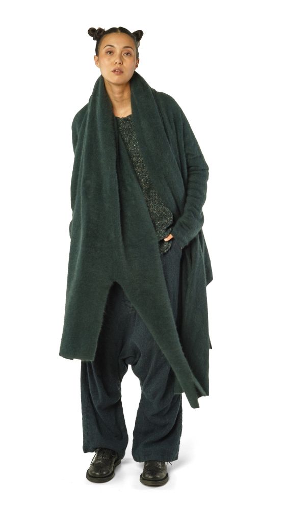 Person trägt oversized grünen Wollmantel mit weitem Schnitt, schwarze Hose und Sneaker, lässig posierend.