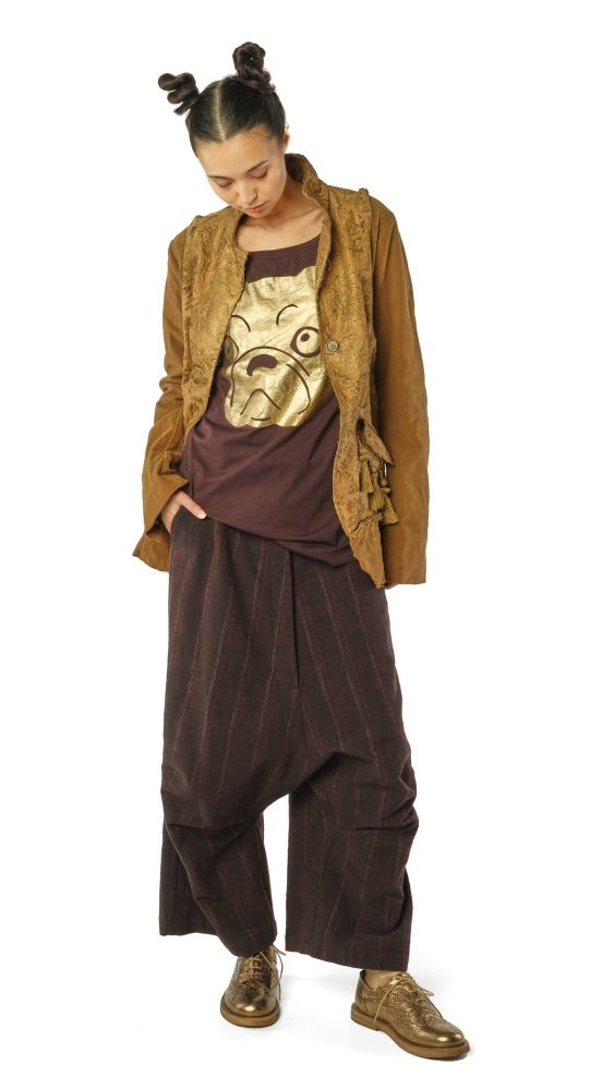 Person trägt maronenfarbene Haremhose, T-Shirt mit goldener Katzenillustration und braunen Cardigan, barfuß in Schuhen.