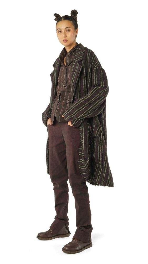 Person trägt oversized gestreifte Jacke, dunkle Hose und Stiefel, Haare zu zwei Hörnern gebunden.
