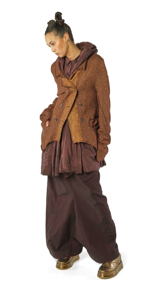 Person trägt oversized braunen Mantel mit weitem Rock und bequemen Hosen, goldene Stiefel.