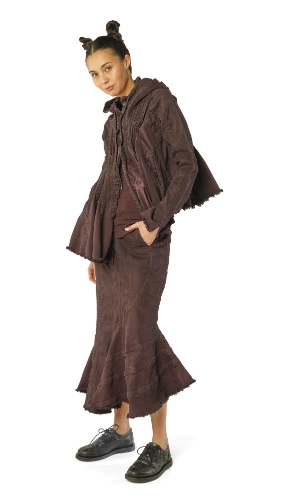 Person trägt maronenfarbenes, langes, weites Outfit mit Kapuze und schwarzen Sneakern.