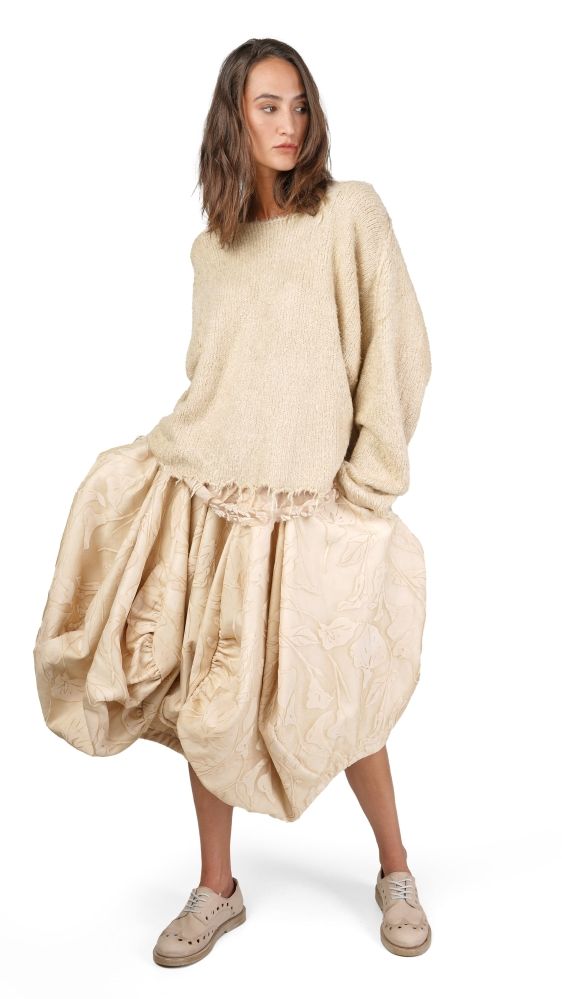 Frau trägt oversized beige Pullover mit weitem, gemustertem Rock und flachen Schuhen.
