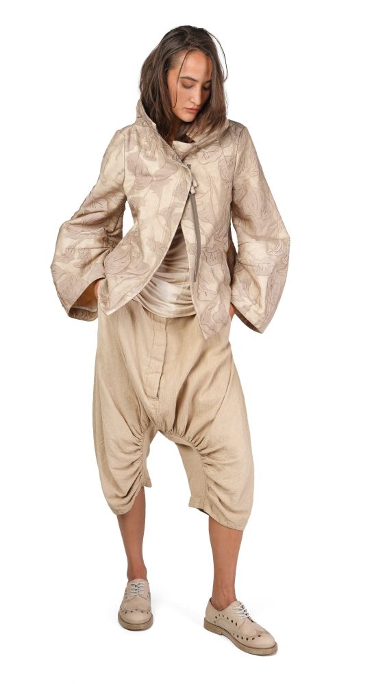 Person trägt beige, oversized Jacke mit Muster und weite Haremhose, barfuß mit Sneakers.