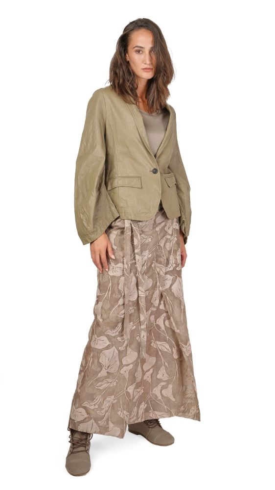 Frau trägt olivfarbene Jacke mit weitem Rock in Naturmuster, beige Bluse, braune Stiefel.
