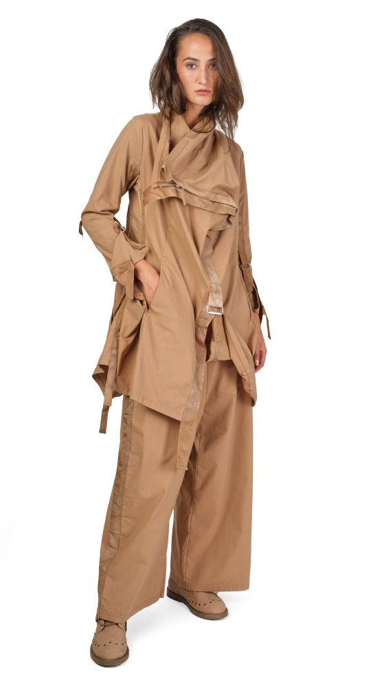 Frau trägt beiges, weit geschnittenes Overalls-Kleid mit weitem Ärmeln und Sandalen.